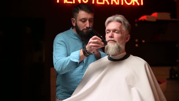 The master in the barbershop evens the beard for a respectable stylish client