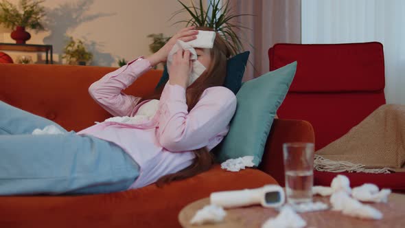 Sick Ill Child Kid Suffering From Cold or Allergy Lying on Home Sofa Sneezes Wipes Snot Into Napkin