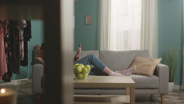 Beautiful Woman Eats a Red Apple Lying on Sofa and and Speaks Via Video Link