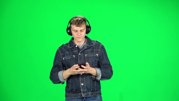 Guy in Big Headphones Goes and Texting with Smartphone on Green Screen at Studio. Slow Motion