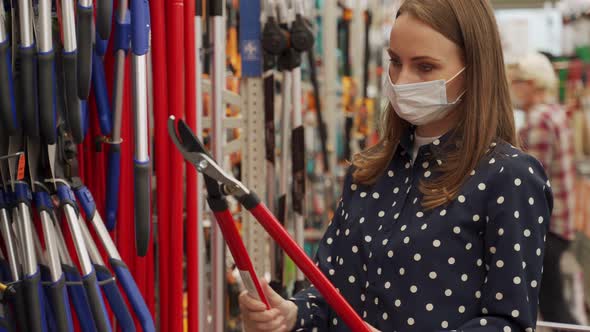 Woman in a Medical Mask Chooses a Pruner in a Garden Store