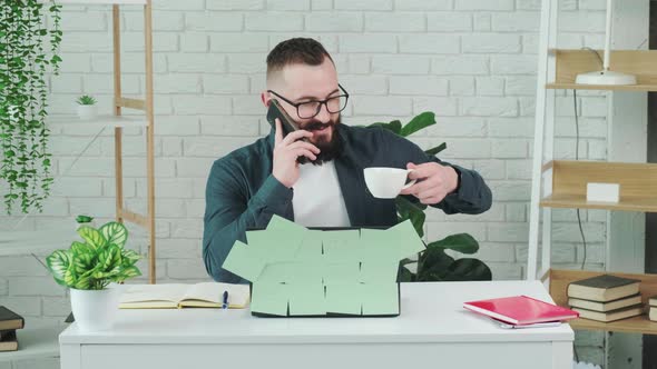 Handsome Bearded Man Drinking Coffee While Talking on a Smart Phone