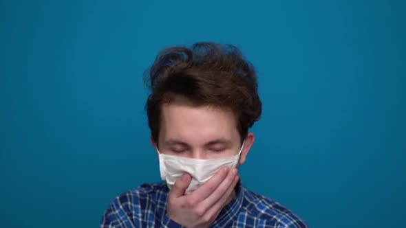 Teenager Coughs in a Mask on a Blue Background