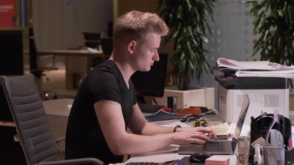 European Young Man Working Uses Laptop Computer, Business At Night Dark Empty Office