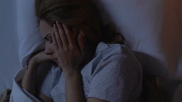 Crying Woman Lying in Bed at Night, Holding Head, Suffering From Migraine