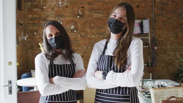 Two caucasian women wearing face masks and aprons, looking at camera