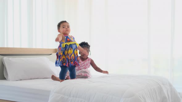 Two African American little girls play together and fun on bed by jumping and also look around