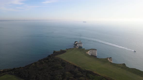 Old Harry Rocks coast and boat sailing on calm sea, county Dorset in England. Aerial forward panoram