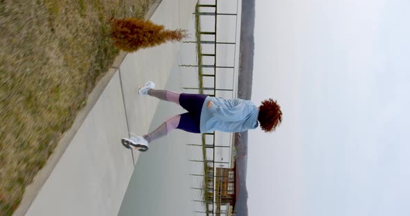 curly girl with red hair runs near the lake along the thuja and turns to the bridge