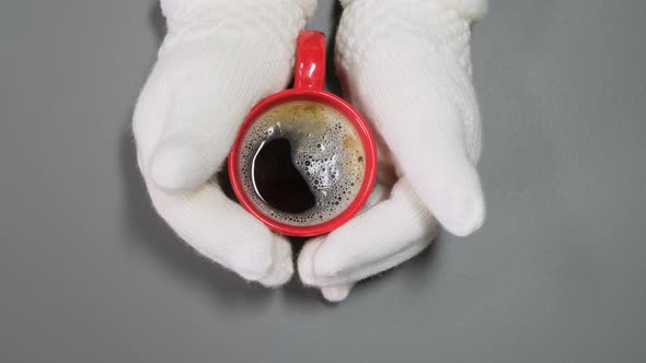 Hands in white mittens and red cup of coffee.