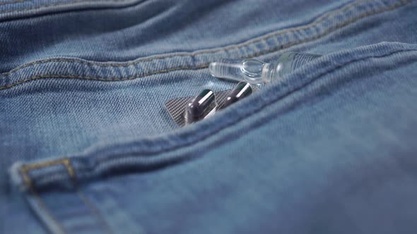 Blister pack with gray and green capsules and an injection ampoule in the pocket of blue jeans. 