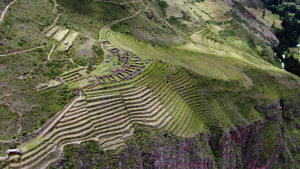 Inca Ruins In Hillside Curved Terraces Overlooking Pisac Old Town In Cusco, Peru. Aerial Pan Right