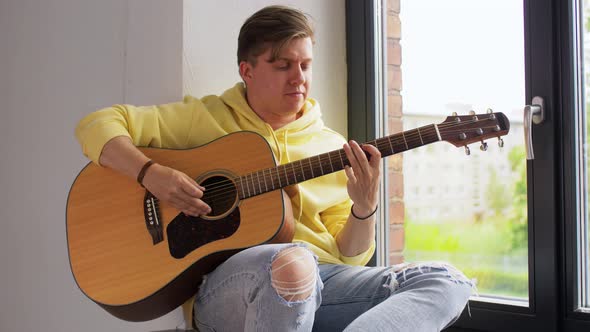 Young Man Playing Guitar Sitting on Windowsill