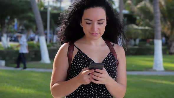 Young Woman or Girl Is Texting Messages on the Phone on a Sunny Day on a Background of Palm Trees
