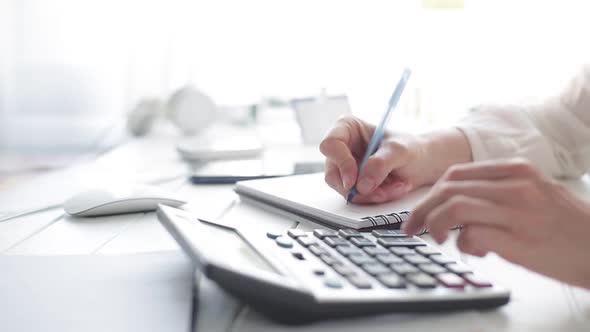 The hands of a financial analyst count on a calculator and write a report.