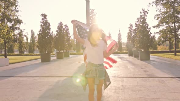 Young Long Haired Caucasian Woman Rides Skateboard with Smile Holds Flag USA