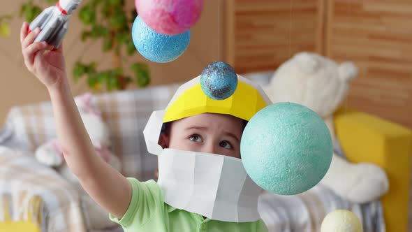 Boy in a space helmet plays with a rocket and planets, showing how he flies among the planets.