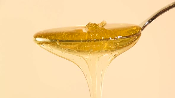 Honey Pouring and Flowing from Metal Spoon over Beige Background