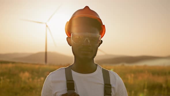 African American Man Standing on Field with Huge Windmills During Summer Sunset