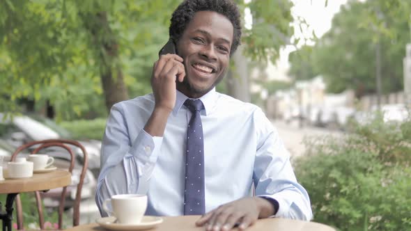 African Businessman Talking on Phone Sitting in Outdoor Cafe