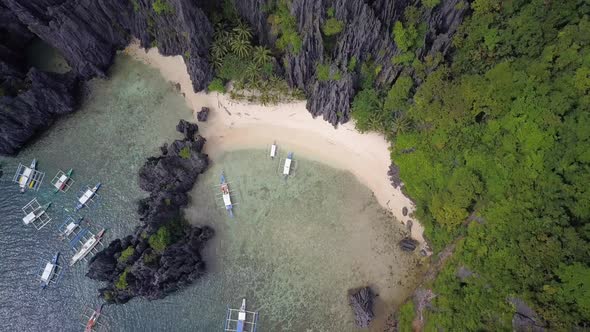 Aerial backwards tracking shot of beach by limestone cliffs at Secret Lagoon in El Nido, Palawan, th