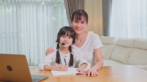 Portrait of Homeschool Asian little Kid looking computer with mother's support and look at camera.