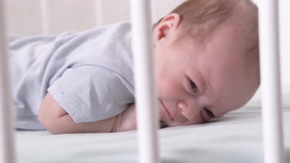 Dissatisfied Crying Upset Sad Newborn Baby Boy Lying in Nursery Cocoon with Blue Clothes on Bed in