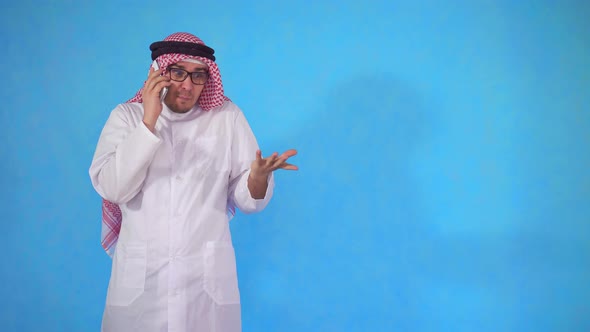 Angry Arab Man Impulsively Talking on the Phone Standing on a Blue Background