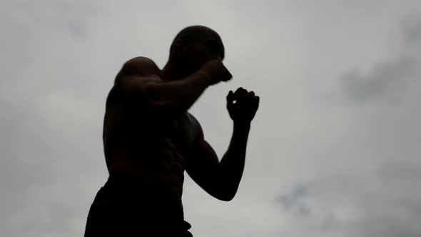 a Male Silhouette with a Bare Torso Trains Against a Light Sky