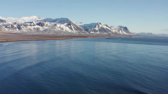 Drone Over Sea Towards Icy Coastline And Snow Covered Mountains