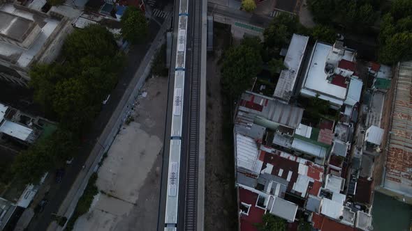 Tilt up of train leaving station revealing Belgrano neighborhood buildings at sunset, Buenos Aires,