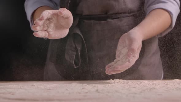 A Woman in a Gray Apron Claps Her Hands and White Wheat Flour Flies in Different Directions Over a