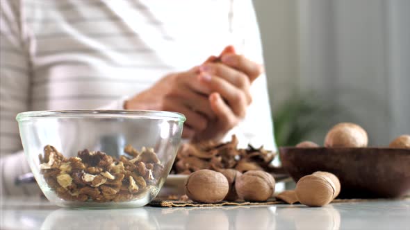 Young Woman Is Cracking a Walnuts and Collecting It in Glass Bowl, Close-up