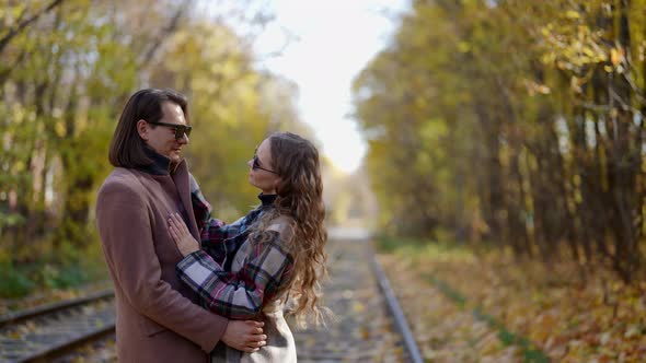 a Man and a Woman in a Coat and Dark Glasses Hugged and Stand on the Rails Against the Background of