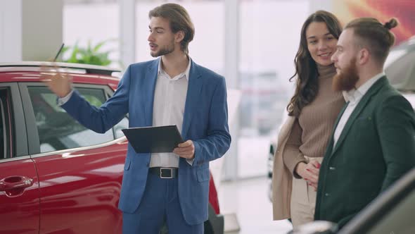 Confident Car Dealer Talking and Gesturing As Happy Young Successful Couple Listening and Smiling