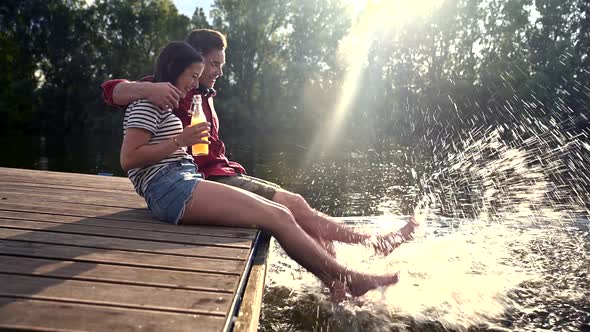 Couple having a drink and splashing with water at lake