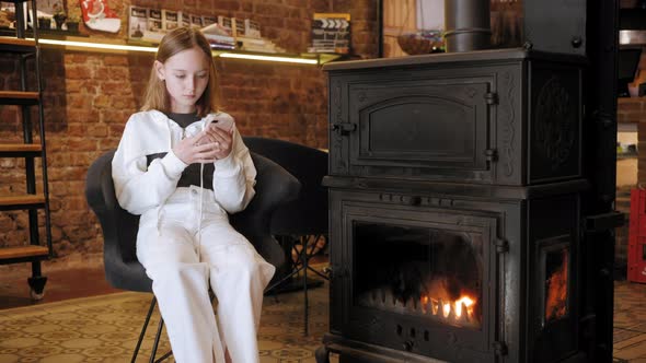 Young Woman Using Mobile Phone Near Fireplace in Cozy Interior