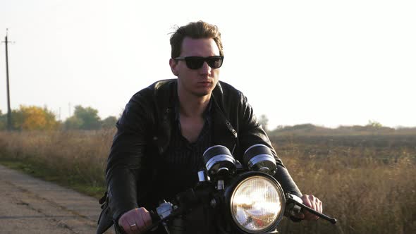 Closeup View of a Stylish Cool Young Man in Sunglasses and Leather Jacket Riding Motorcycle on a