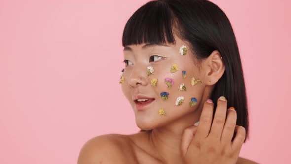 A close-up view of a brunette asian woman posing with colorful flowers on her face