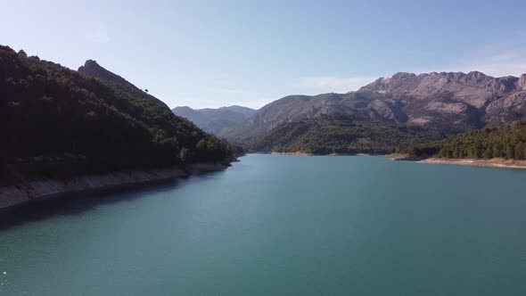 Guadalest water reservoir with coastline surrounded by mountains and forest on a sunny day with blue