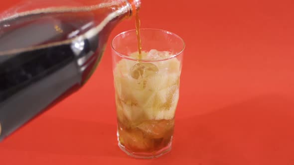 Pouring a cola drink into a glass with ice cubes on the side.