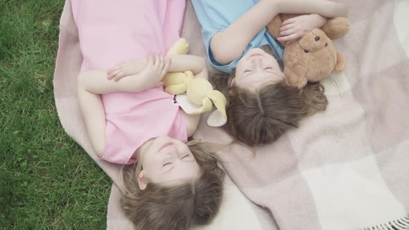 Camera Moves Around Charming Cute Girls Sleeping with Toys Outdoors on Blanket. Top View of