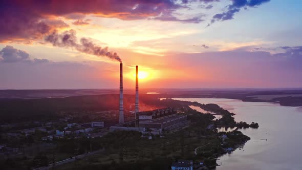 Beautiful sunset with power plant on front view. Red and yellow sky above river.