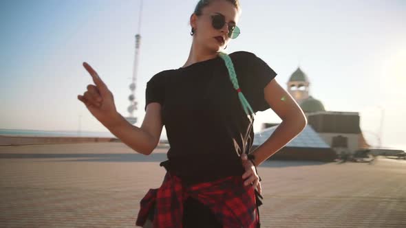 Young Stylish Funky Girl with Green Hair Riding Roller Skates and Dancing Near Sea Port During