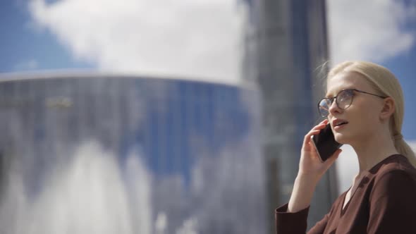 A Business Woman Walks Past Highrise Buildings and Speaks on the Phone