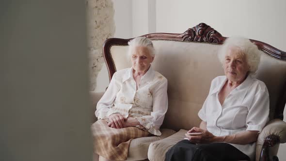 Two Elegant Grandmothers Sitting on a Sofa in Light Room