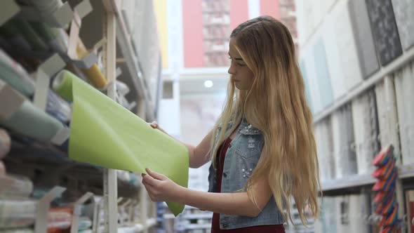 Young Single Woman is Taking From Shelf in a Shop a Roll of Wallcovering