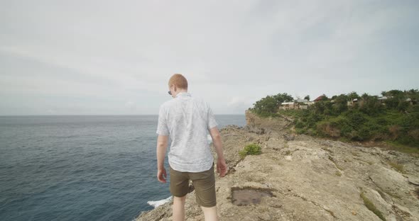 Close Up Following Shot of a Man with Ginger Hair Walking on the Cliff Above the Ocean Alongside