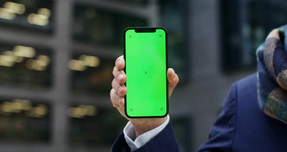 A Warmly Dressed Man Holds a Green Screen Phone