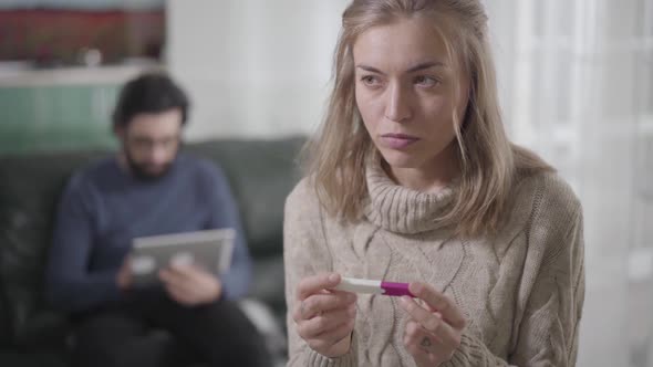 Thoughtful Blond Caucasian Girl with Brown Eyes Holding Pregnancy Test and Looking Back at Man